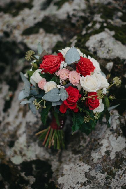 A floral bouquet arranged with red roses, white roses, and light pink spray roses, interspersed with silvery-blue eucalyptus leaves and green foliage. The flowers are freshly cut, showcasing vibrant, 